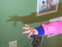 A child uses her hand to make shadow puppets on the wall.